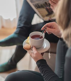 A woman is having a cup of tea; a man is reading
