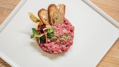 Beef tartare with herbs, berries, physalis and crispy bread on a white, elegant plate.