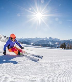 Due sciatori scendono su pista fresca con sole splendente e panorama alpino mozzafiato.