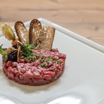 Beef tartare with herbs, berries, physalis and crispy bread on a white, elegant plate.