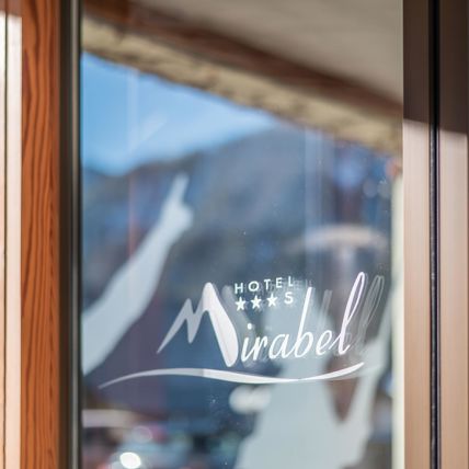 Glass front with Hotel Mirabel logo; mountains and blue sky reflected in the background.