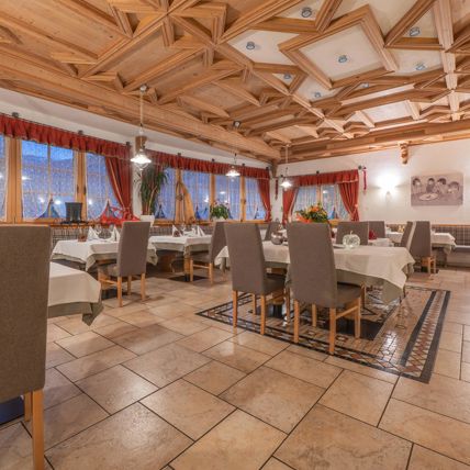 Luminosa e accogliente sala da pranzo con soffitto in legno, grandi finestre, tavoli apparecchiati e sedie imbottite.
