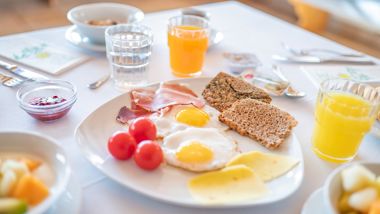 Hearty breakfast with eggs, cheese, ham, muesli, juice, croissant, and fruit on a set table.