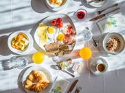Reich gedeckter Frühstückstisch mit Eiern, Käse, Schinken, Müsli, Saft, Croissant und Obst