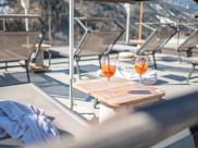 Zwei Gläser Aperol auf einem Tisch zwischen Sonnenliegen auf einer Panoramaterrasse im Winter.