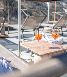 Two glasses of Aperol on a small table between loungers on a panoramic winter terrace.