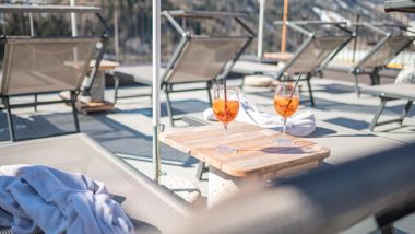 Two glasses of Aperol on a small table between loungers on a panoramic winter terrace.