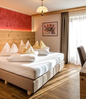 Cozy double room with wooden furniture, red accent wall, desk, TV and balcony access.