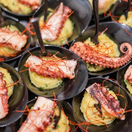 Gegrillter Oktopus auf Kartoffelpüree mit Schnittlauch, garniert mit Chilifäden in schwarzen Schalen.